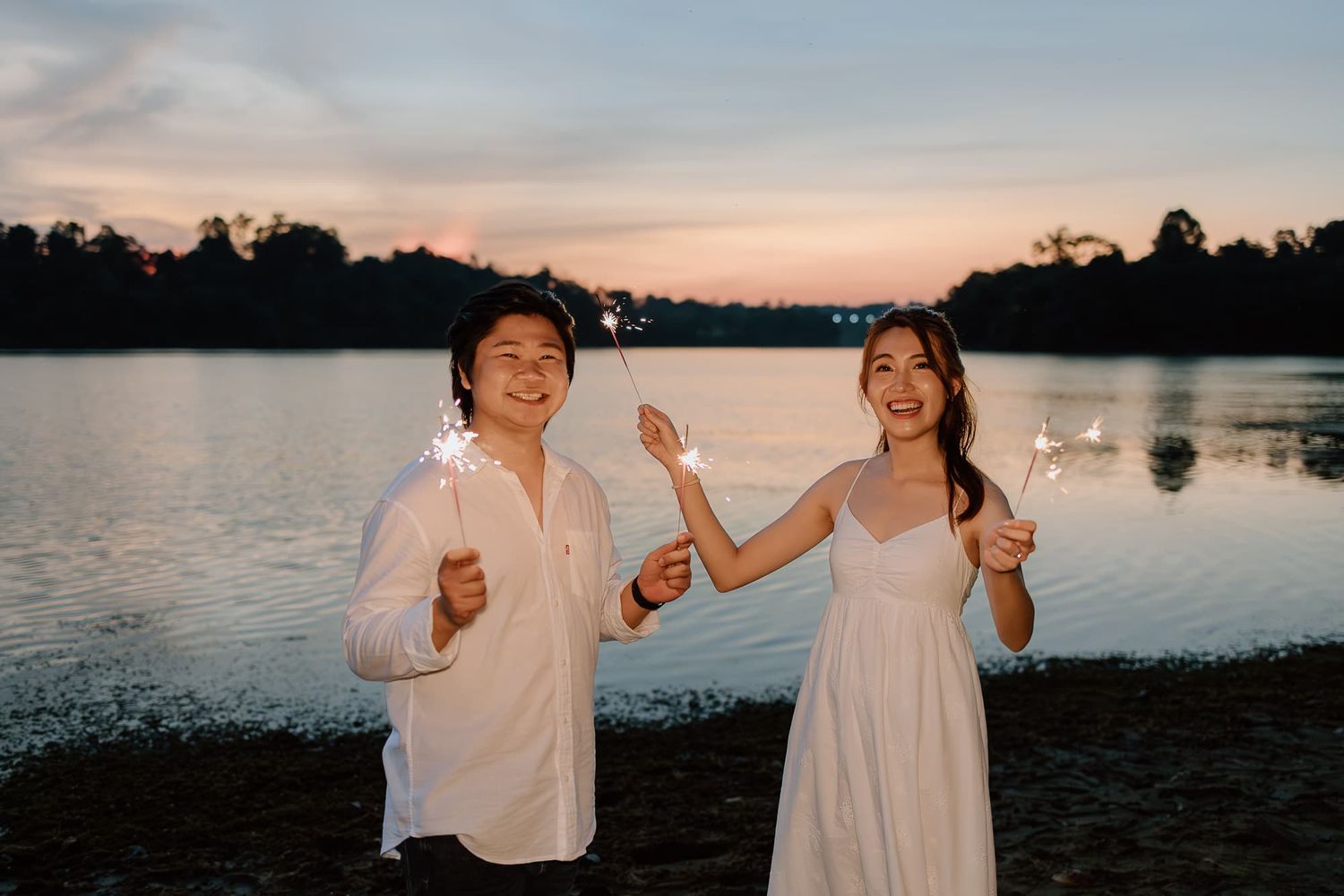 Couple celebrating at sunset by lake in matching white outfits.