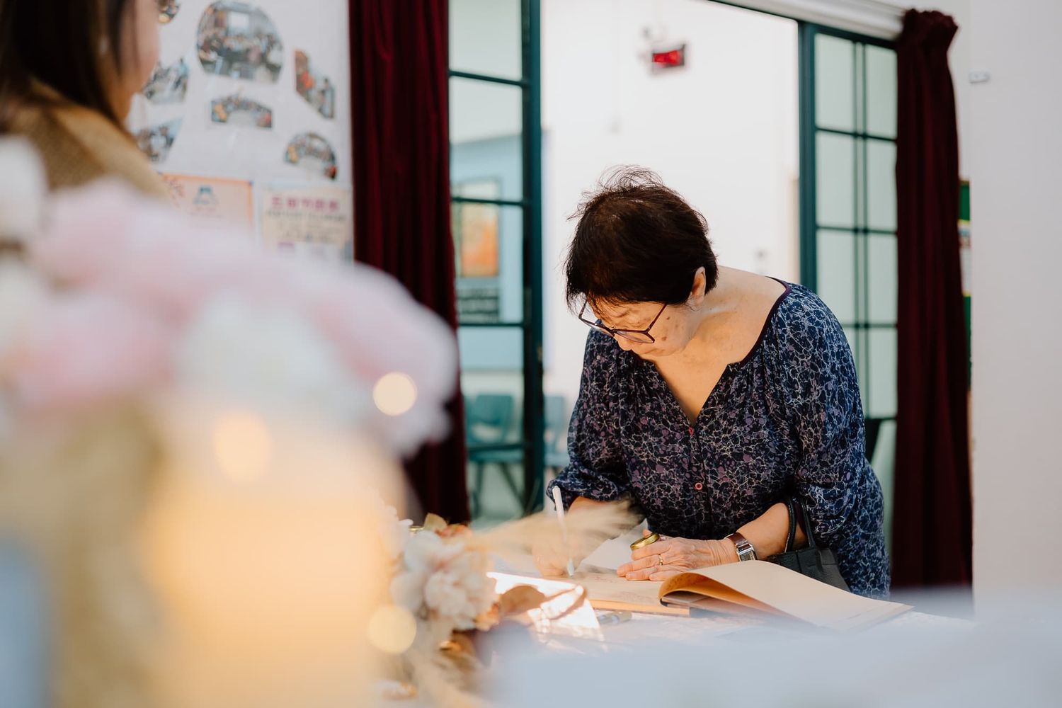 Person signing a guestbook at an event with decorative candles and flowers.