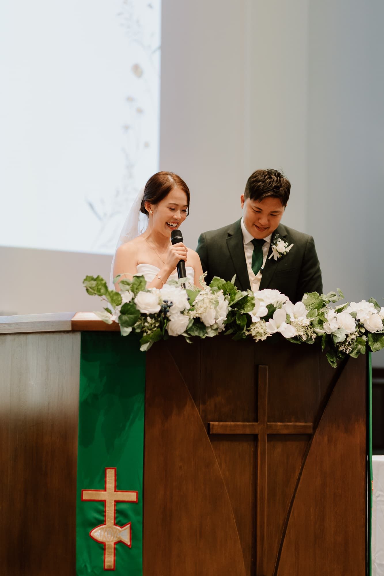 Wedding ceremony altar decorated with white flowers and a wooden cross in a modern church setting.