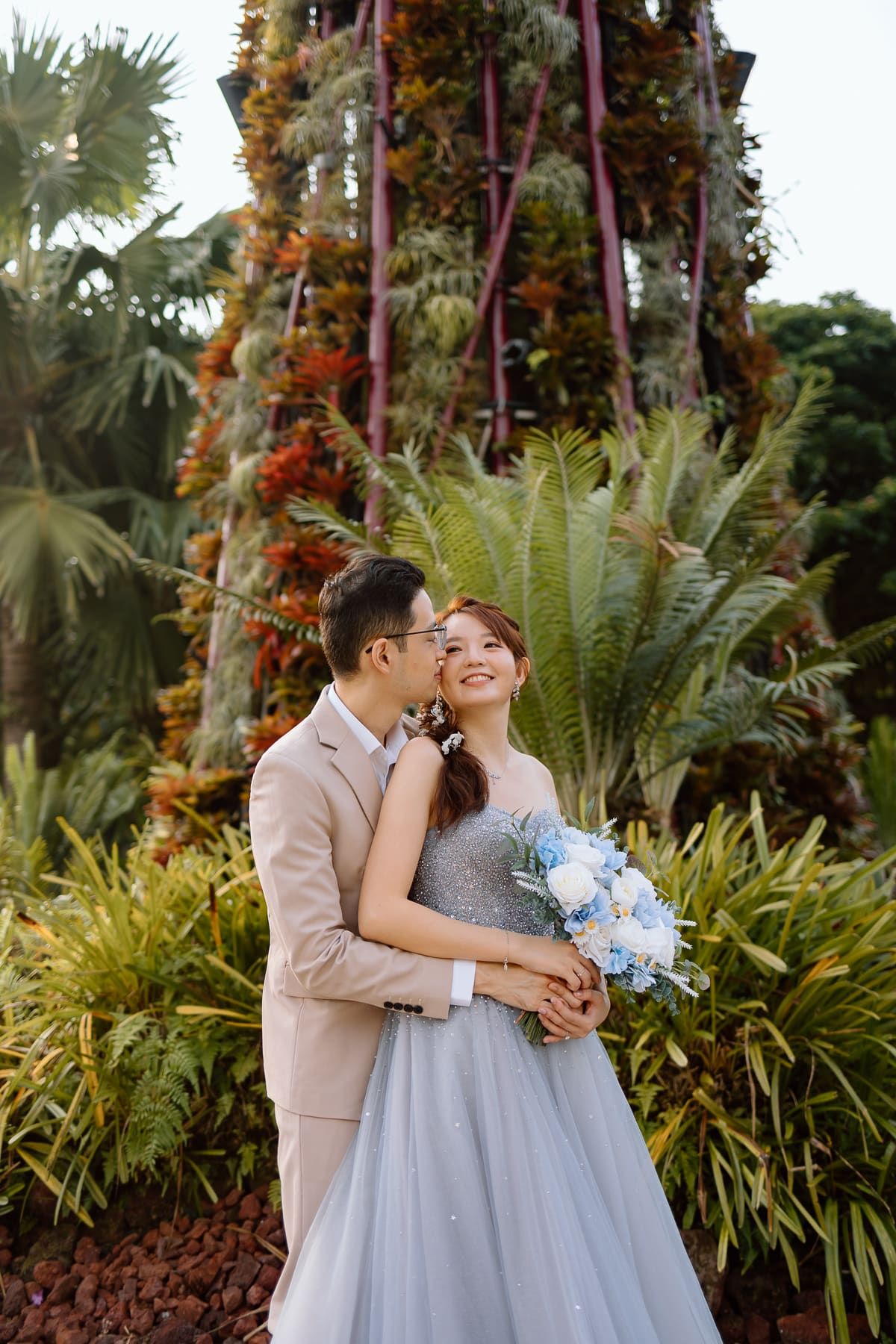 A romantic moment captured in front of a towering vertical garden with tropical plants.