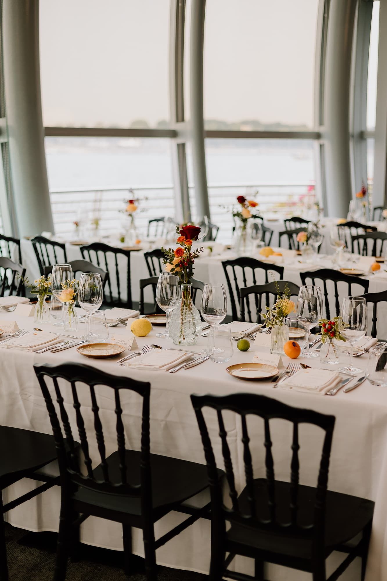 Elegant wedding reception tables set with white linens and black chairs in a modern venue.
