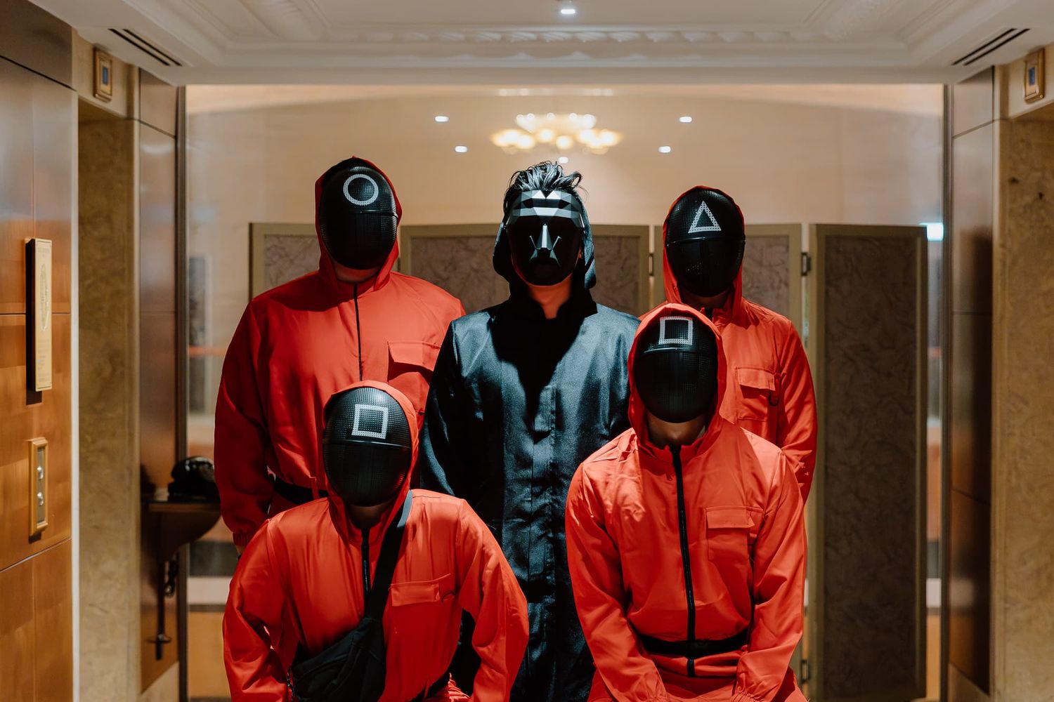 Group wearing matching red jumpsuits and black caps posing in a corridor.
