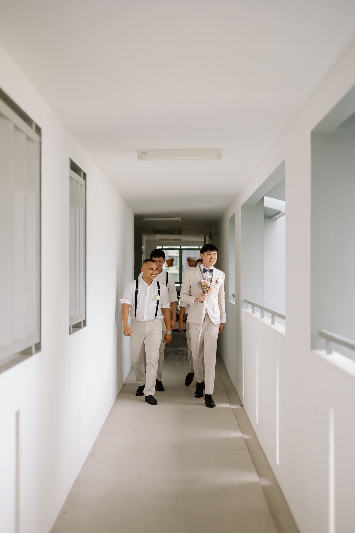 Wedding party members walk through a minimalist white hallway during preparations.