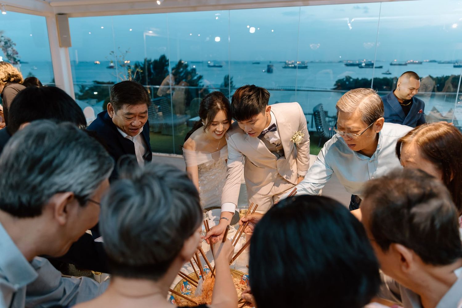 Wedding reception guests seated at tables with waterfront views through large windows.