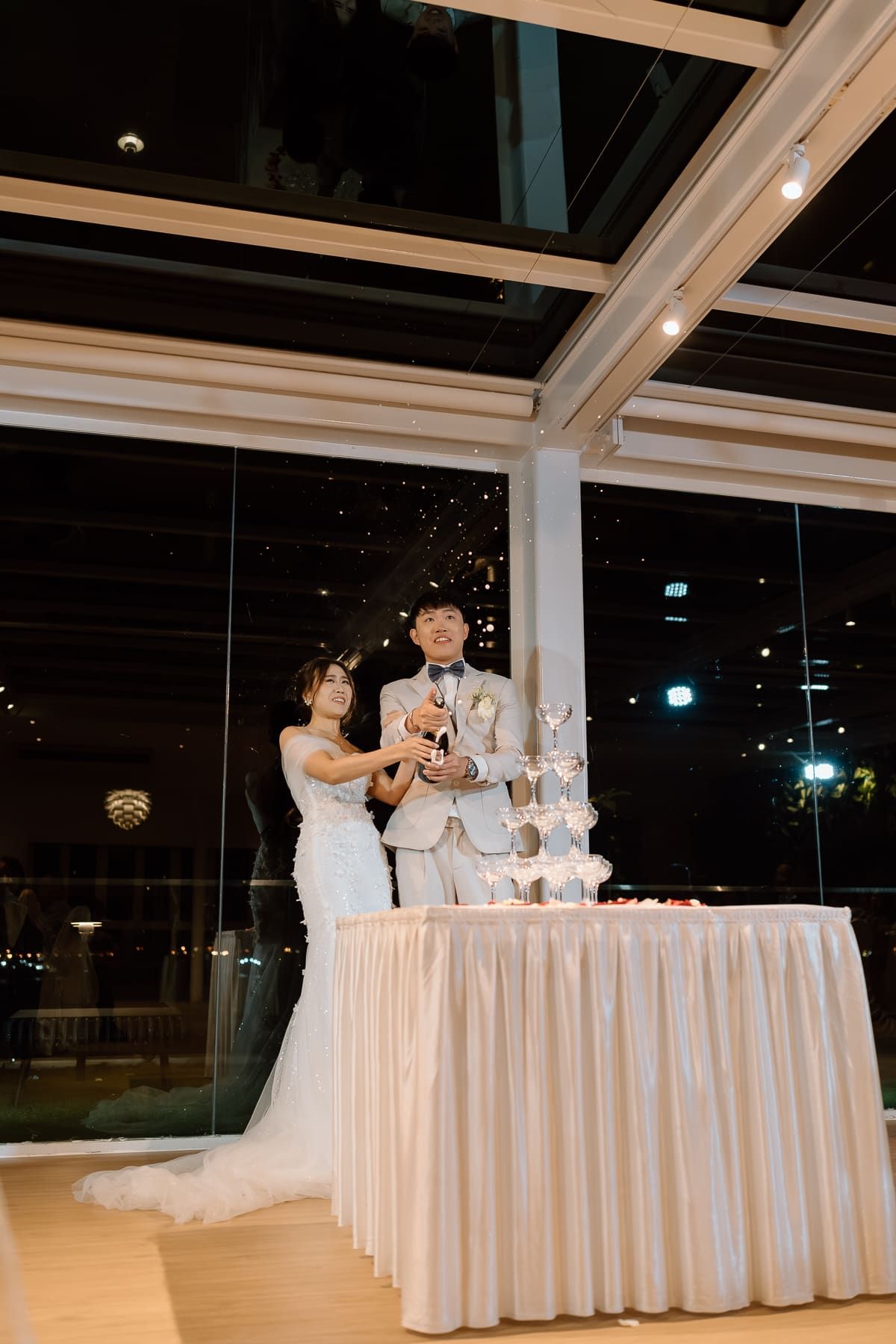 Couple cutting their wedding cake at an elegant reception with a champagne tower and draped white table.