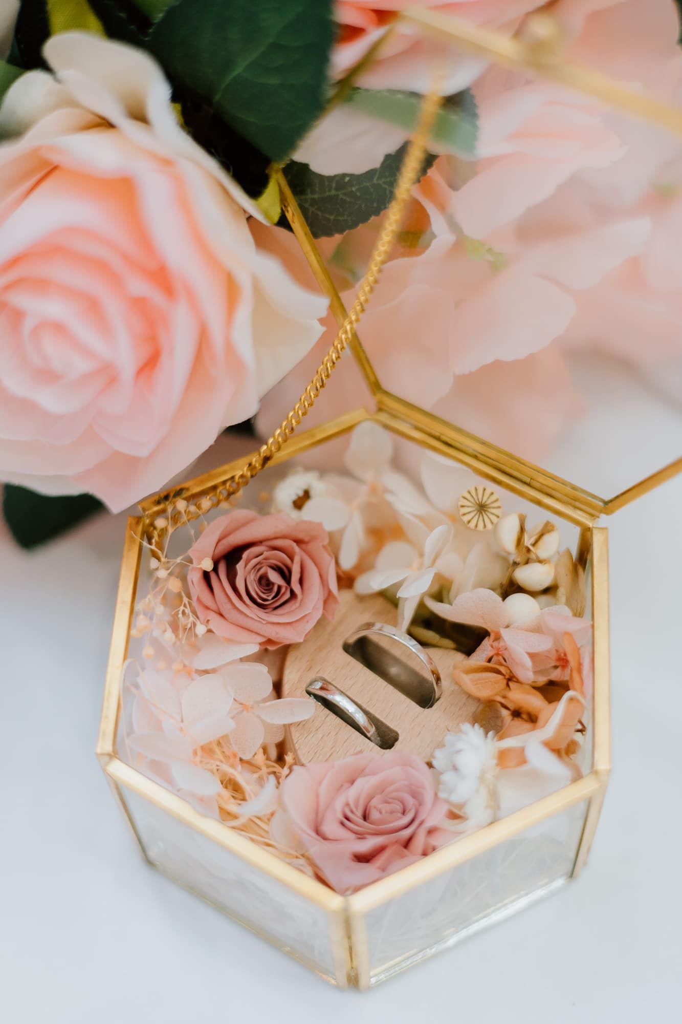 Gold hexagonal ring box filled with delicate pink roses and floral decorations.