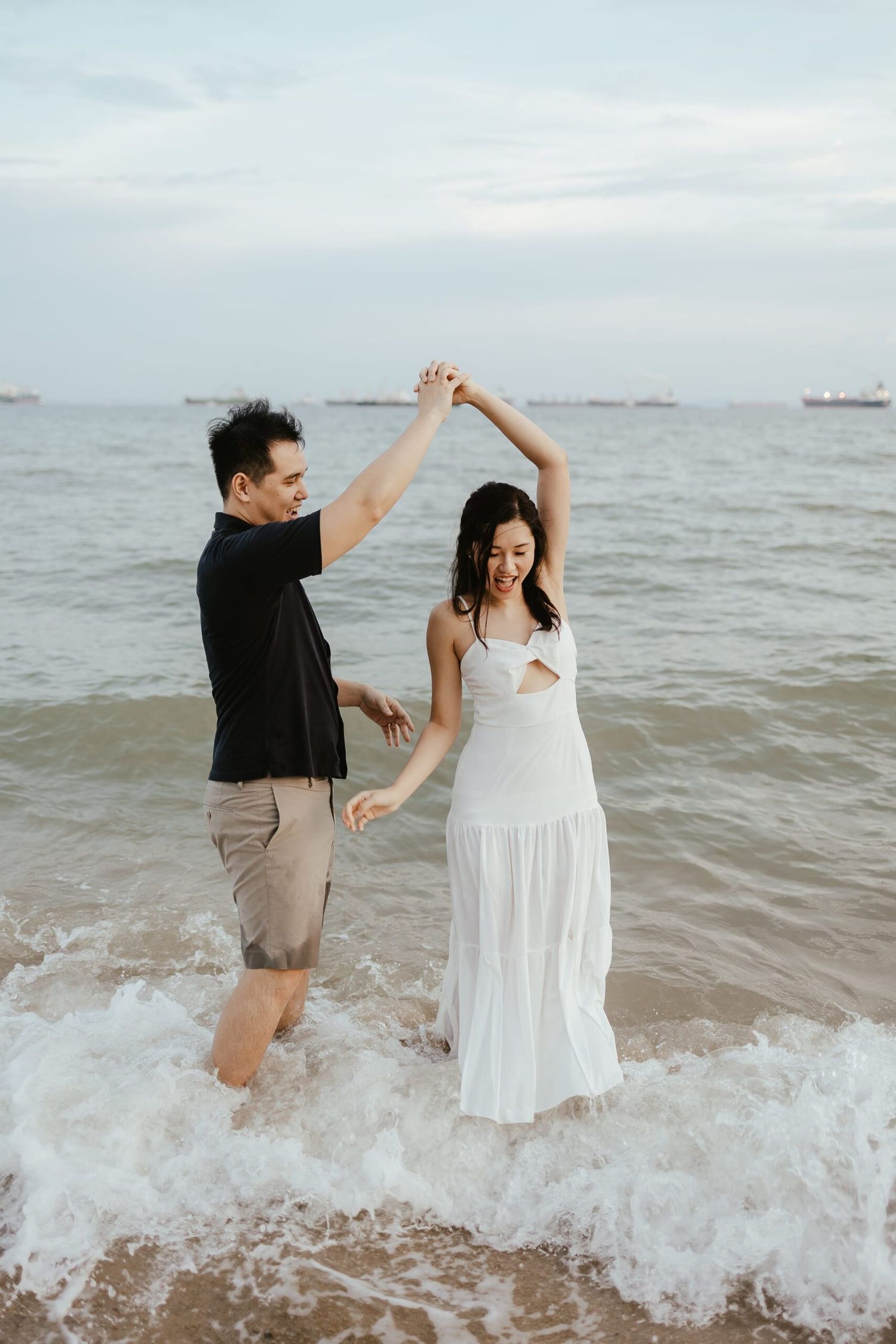 A couple dances in the ocean waves, with ships visible on the horizon.
