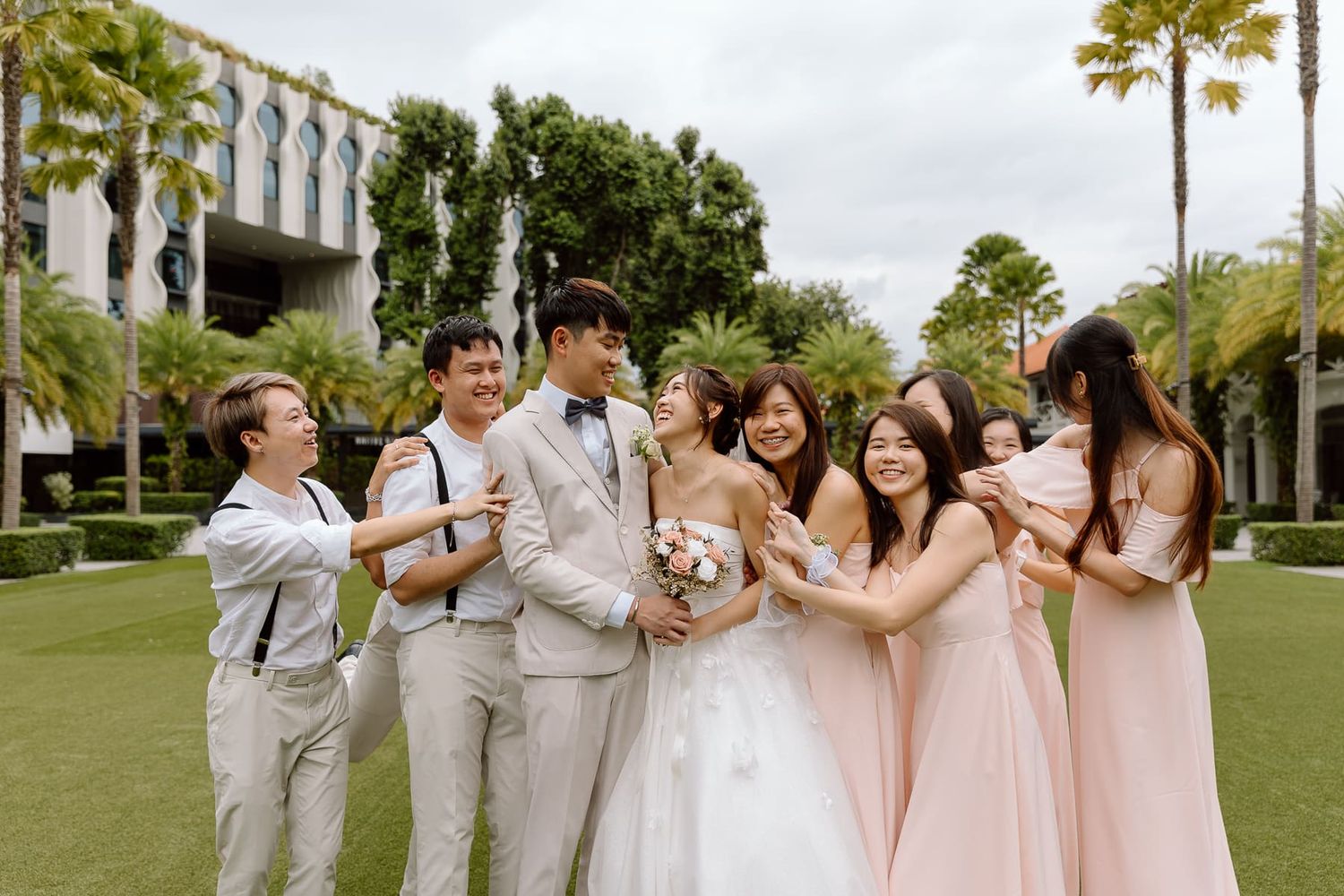 Bridal party celebrating outdoors with bridesmaids in pink dresses and groomsmen in light grey suits.