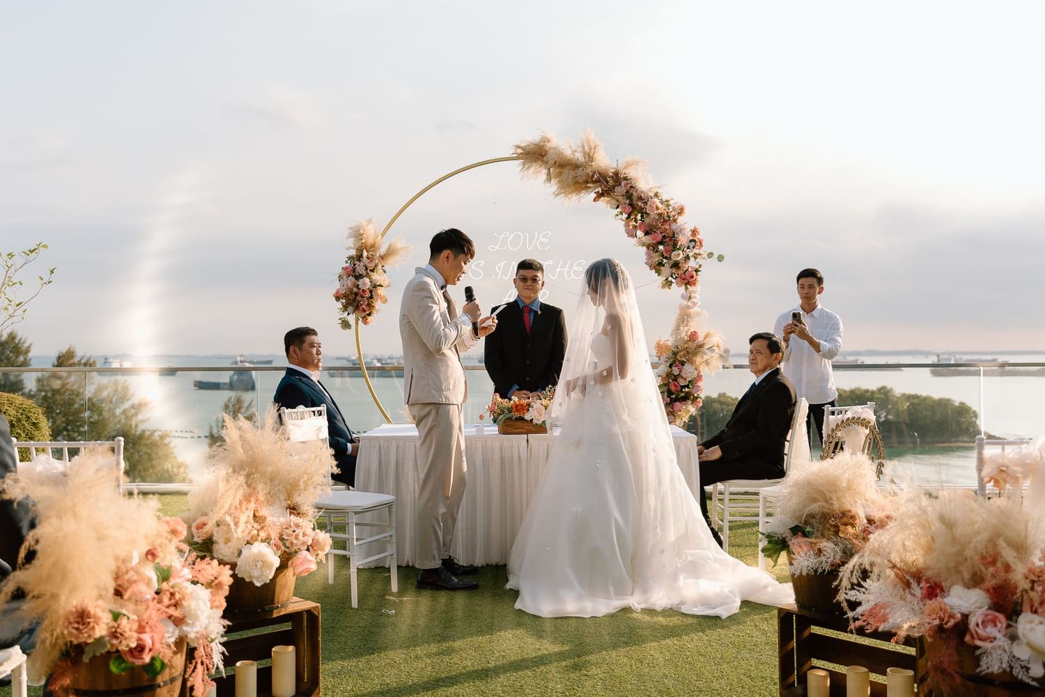 Sunset wedding ceremony on a rooftop with a curved floral arch and pink floral decorations.