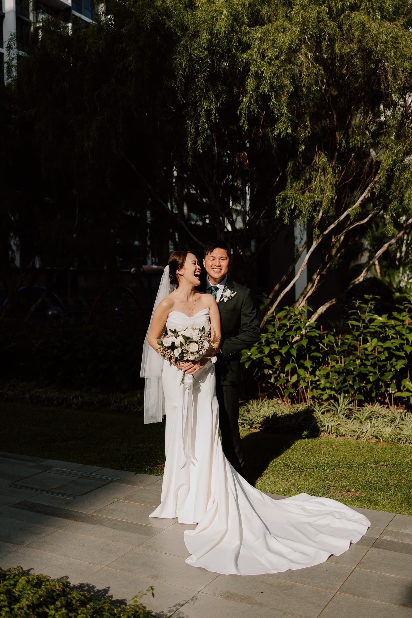 Bride in flowing white dress poses with wedding party on outdoor walkway.