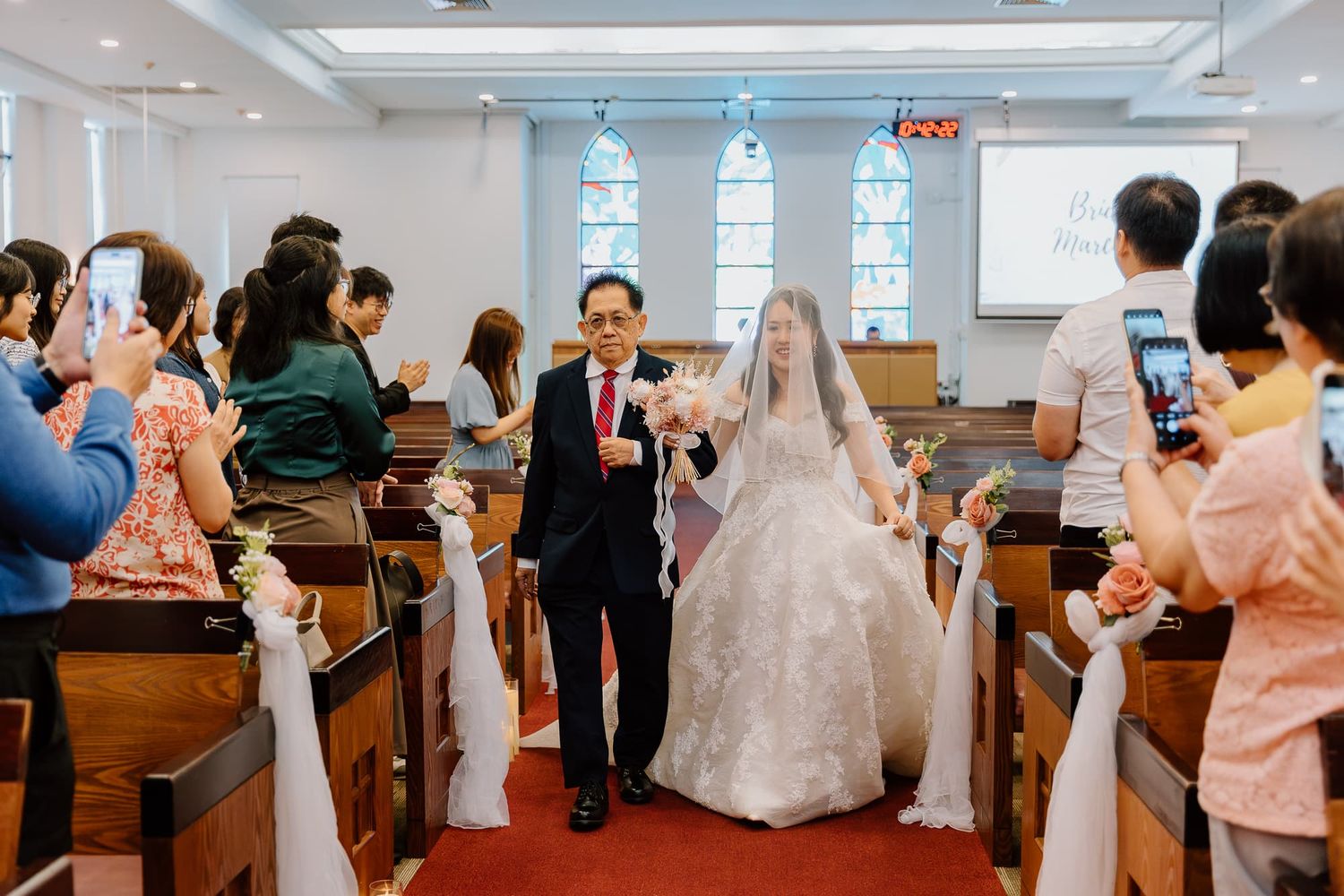 A wedding procession walking down the aisle of a modern church with guests seated in wooden pews.