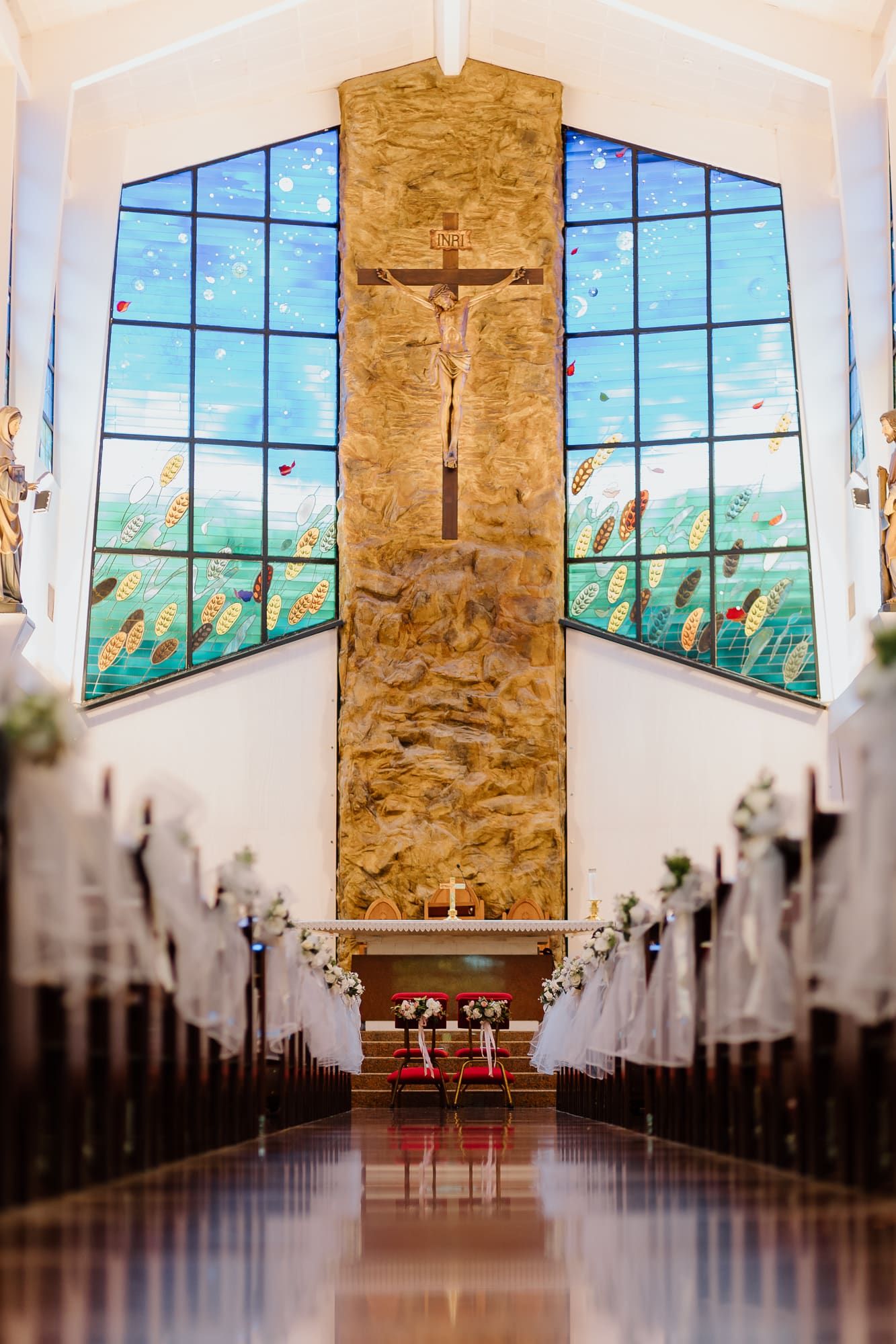 Panoramic view of a modern church interior with stone walls, stained glass windows, and pews leading to a crucifix altar.