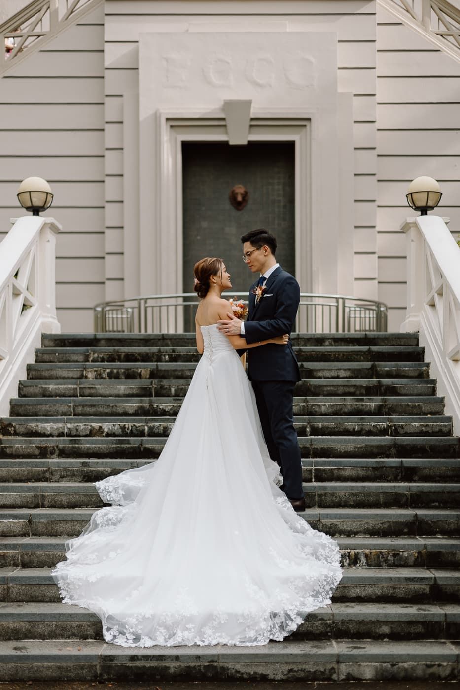 Wedding couple shares intimate moment on grand staircase with beautiful white gown train cascading down steps.