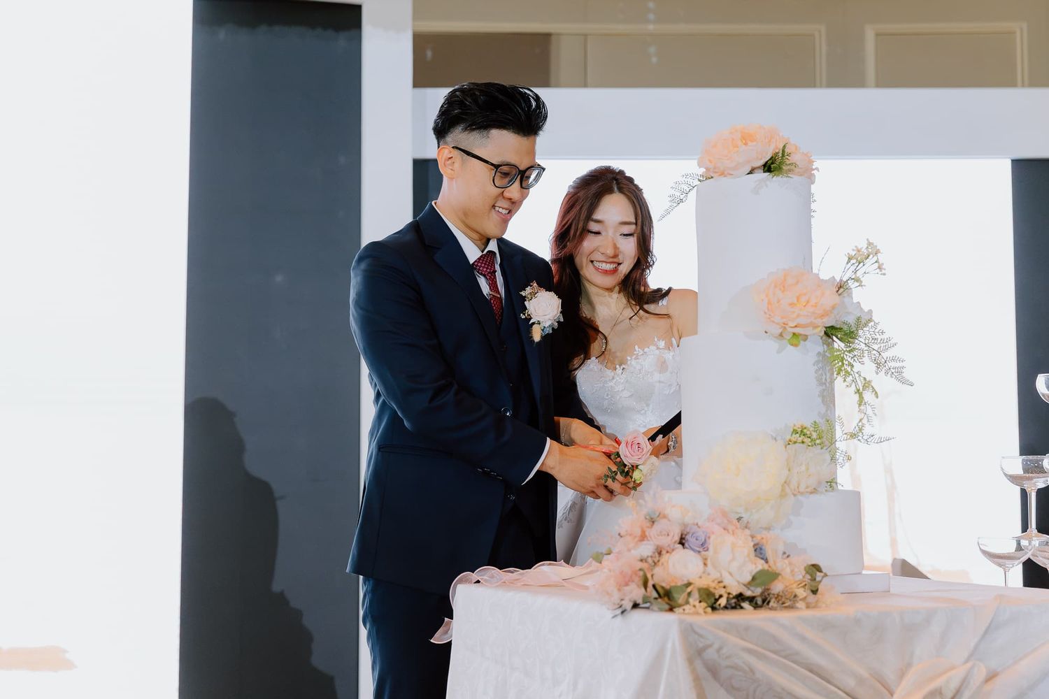 Wedding cake cutting ceremony in an elegantly decorated venue with white floral accents.