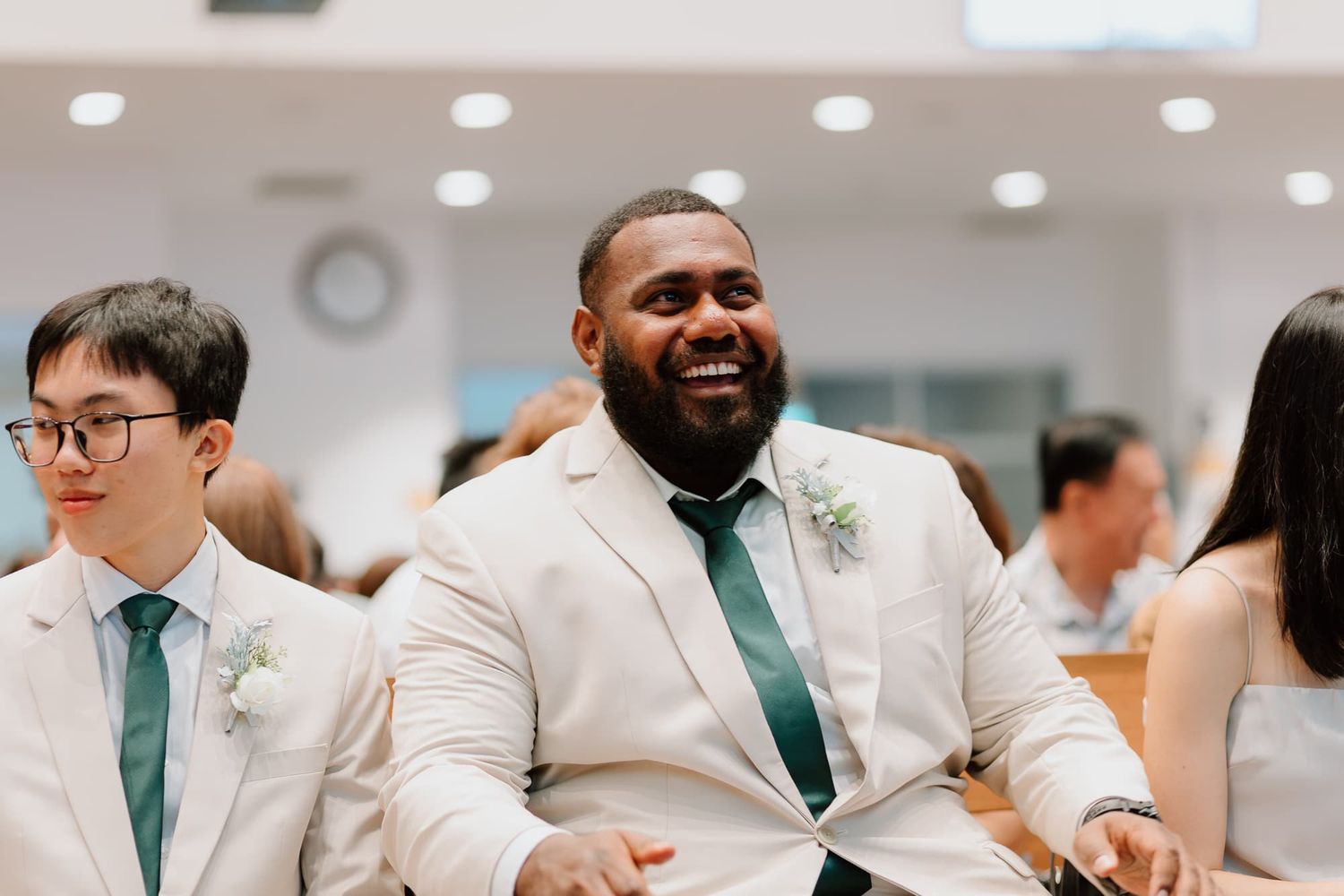 Wedding ceremony guests smile and laugh during joyful celebration in bright indoor venue.