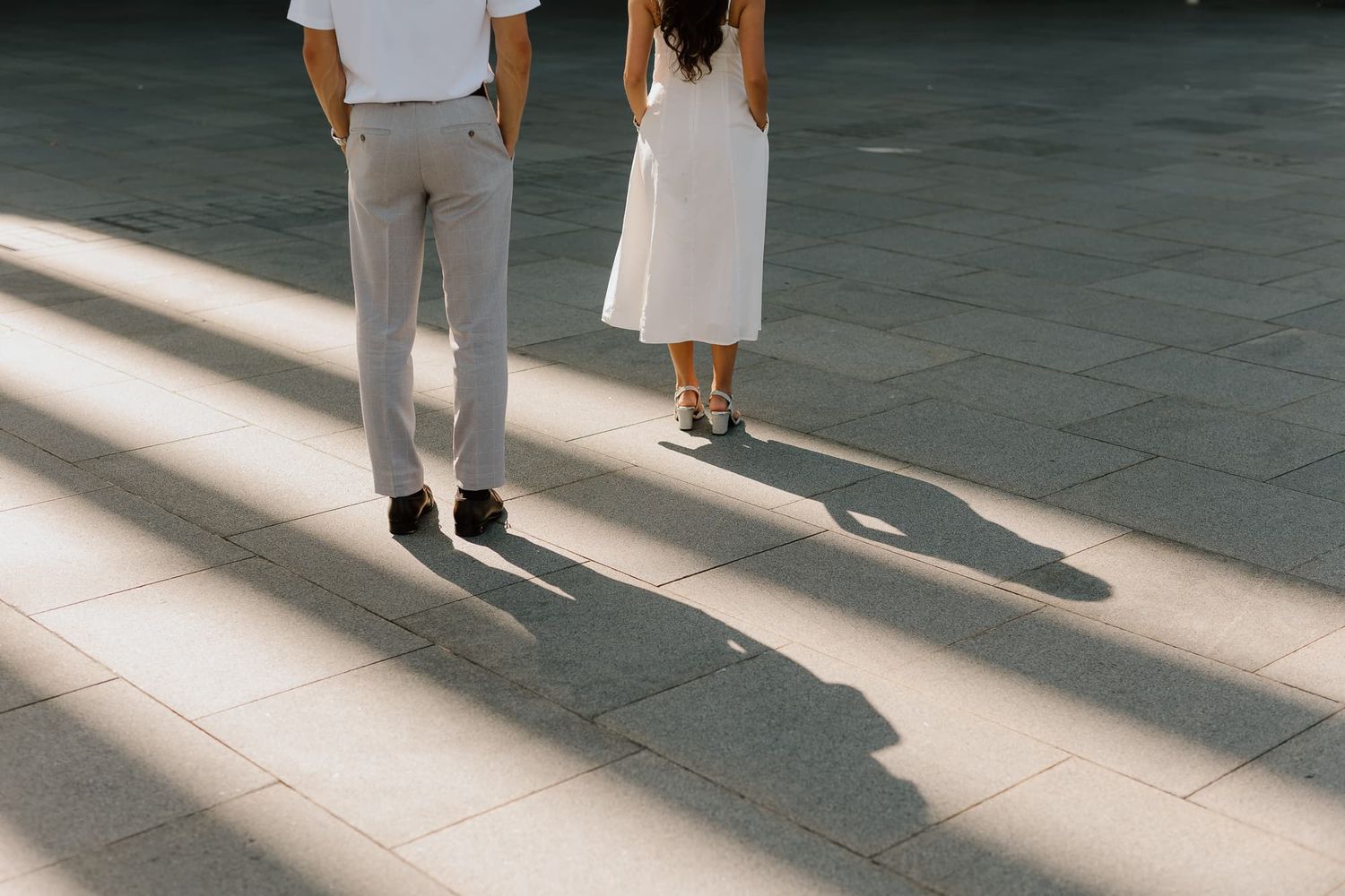 A couple casting long shadows on a tiled floor in minimalist artistic composition.