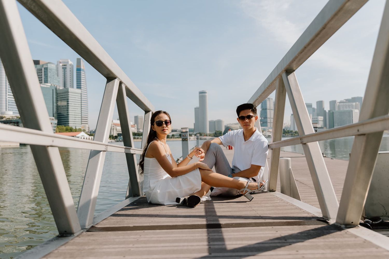 Couple enjoying drinks while sitting on modern waterfront bridge with city views.