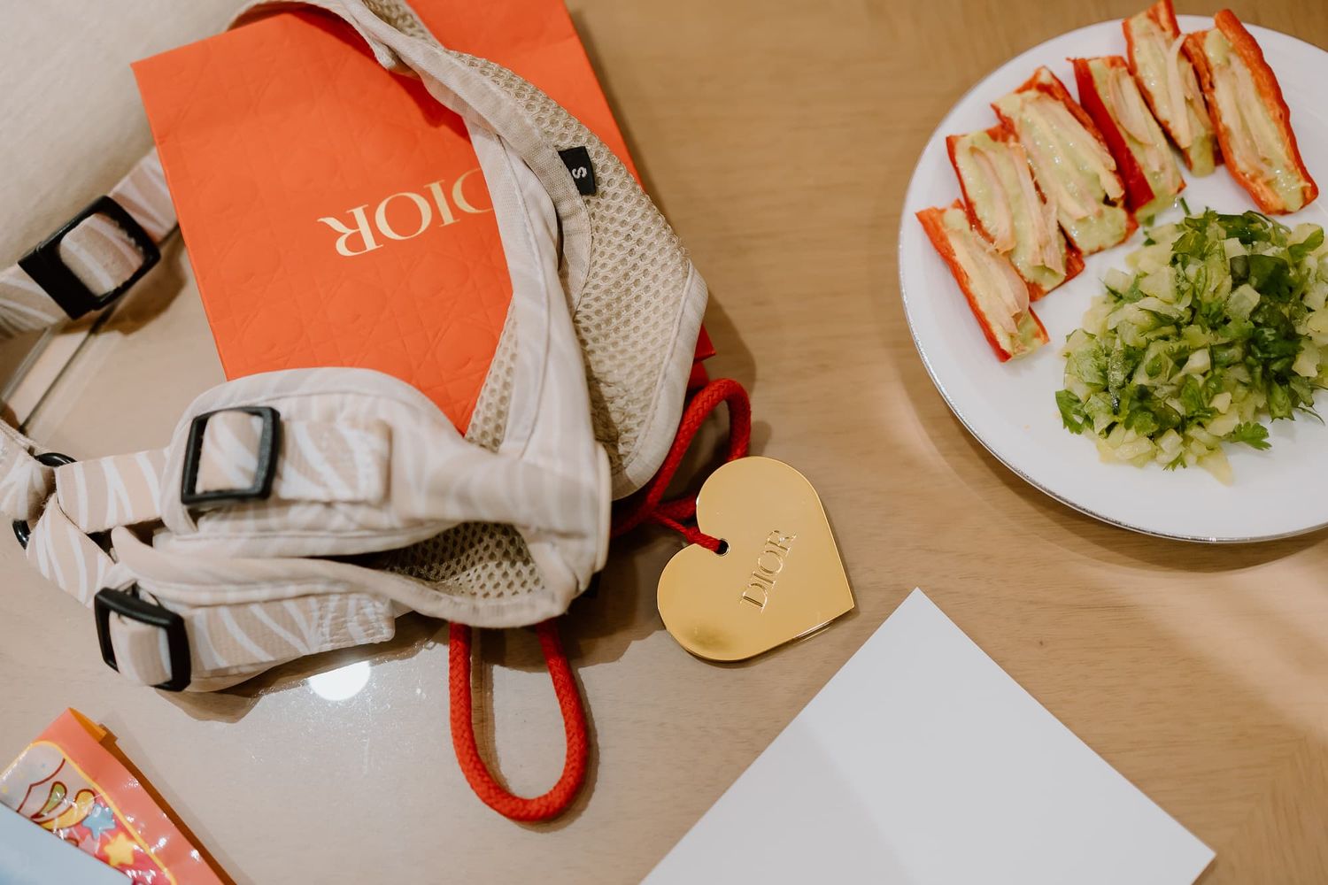 Flatlay of Dior shopping bag next to sandwiches and salad on white surface.