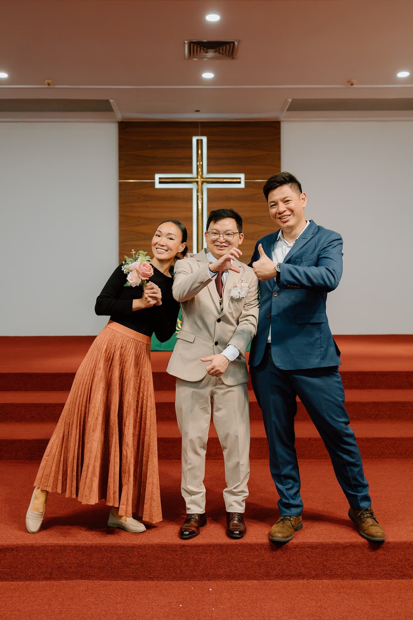 Three people posing playfully in front of an illuminated cross in a church.