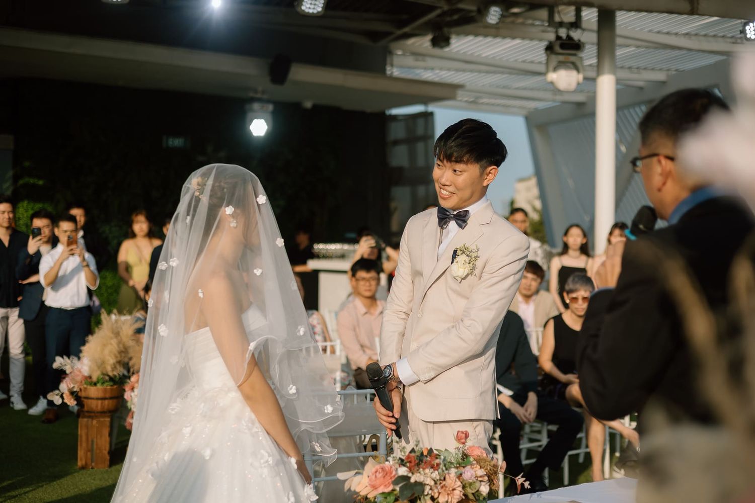 A wedding ceremony taking place at night under overhead lighting with guests watching.