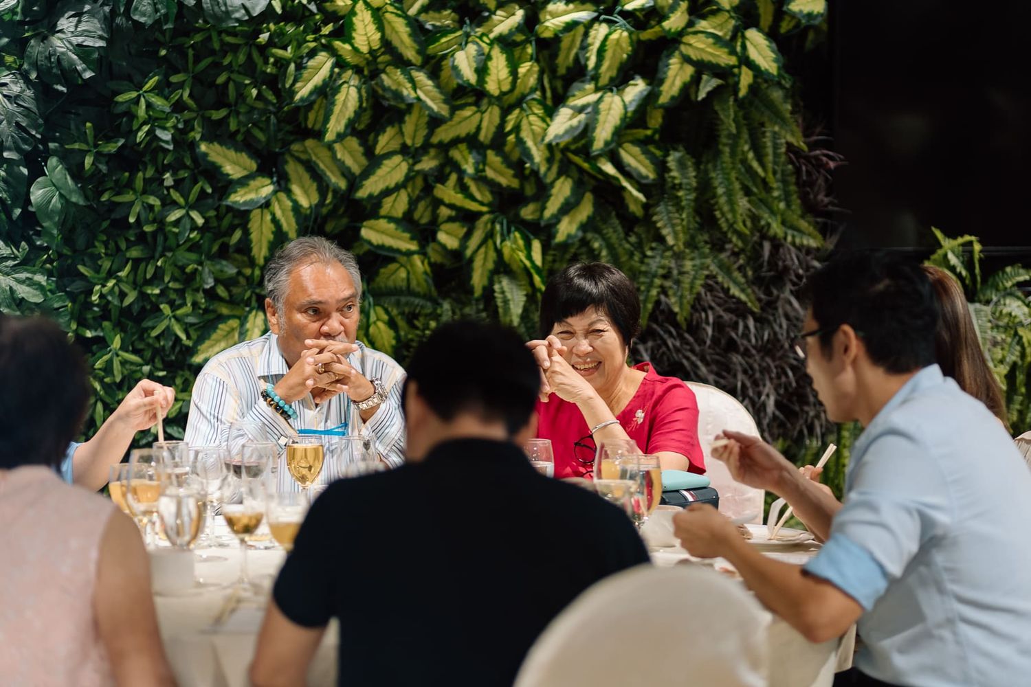 Outdoor wedding reception with lush green foliage backdrop and dining setup.