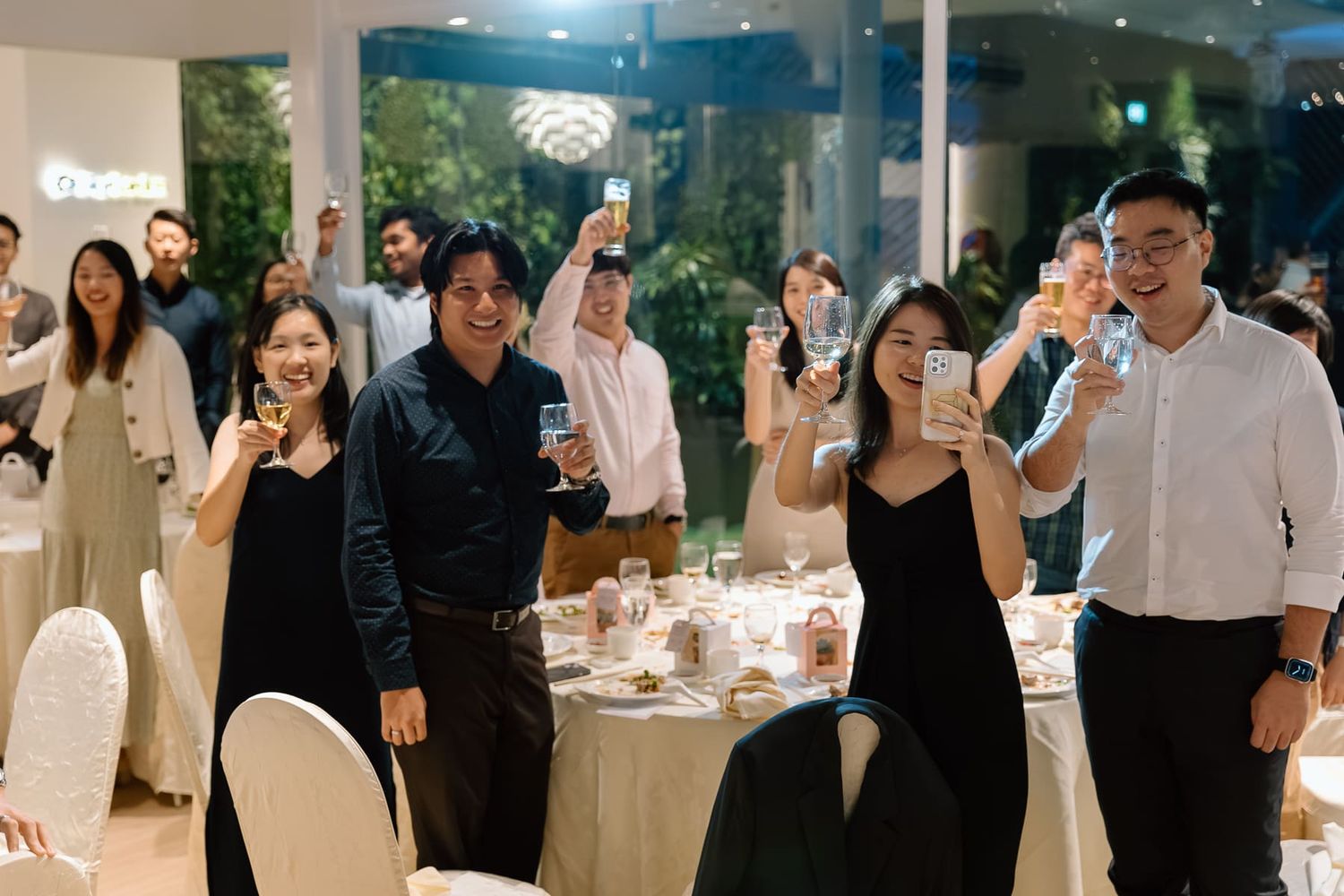 Guests in formal attire raise their glasses for a toast during an elegant wedding reception.