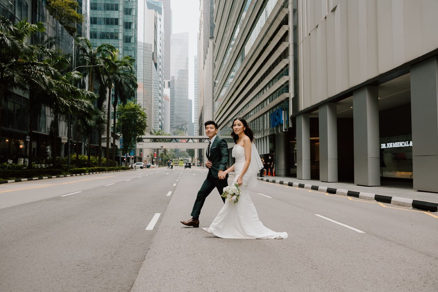 A wedding couple poses playfully in the middle of an urban street lined with modern buildings.