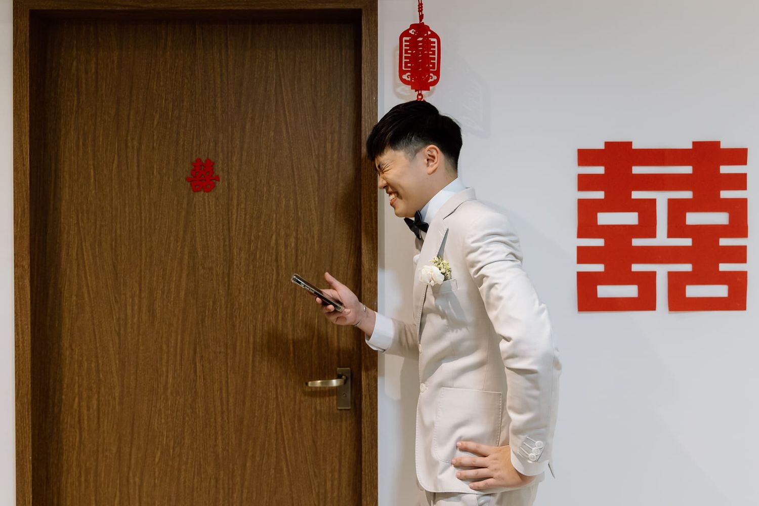 Traditional Chinese double happiness symbol hangs beside doorway with person checking phone.