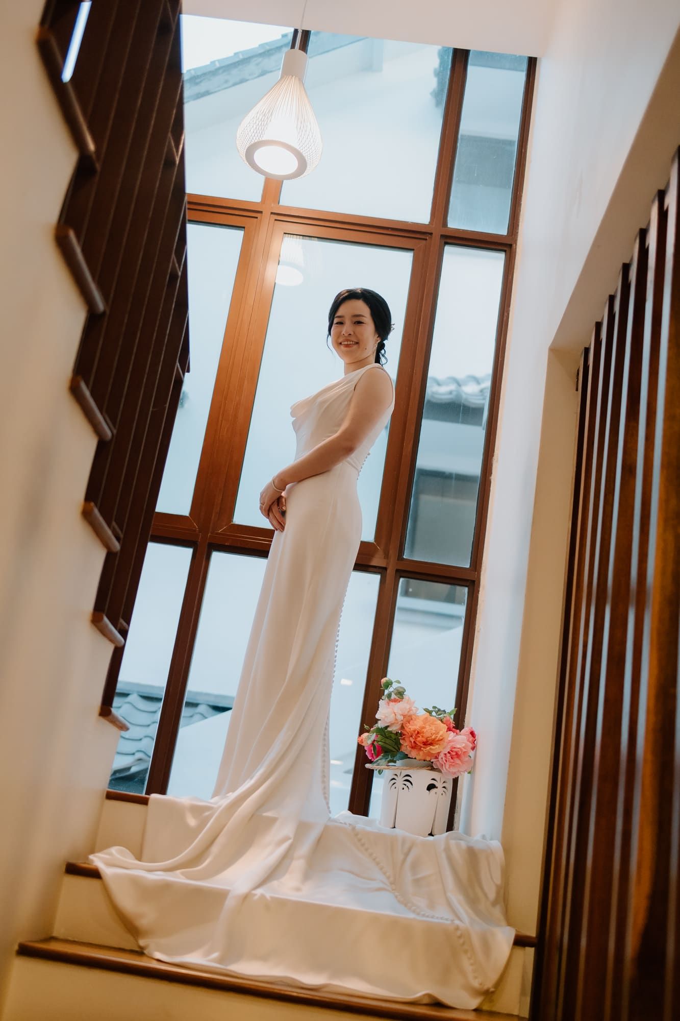 A wedding dress hangs elegantly by a window in a bright interior space with wooden trim.