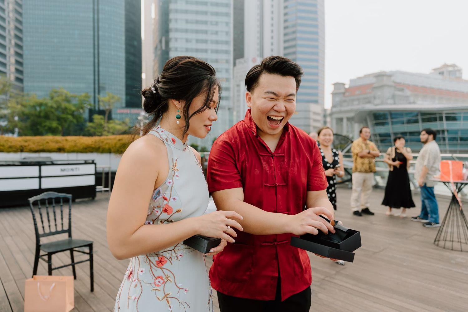 A couple shares a candid moment on a rooftop deck with city buildings in the background.