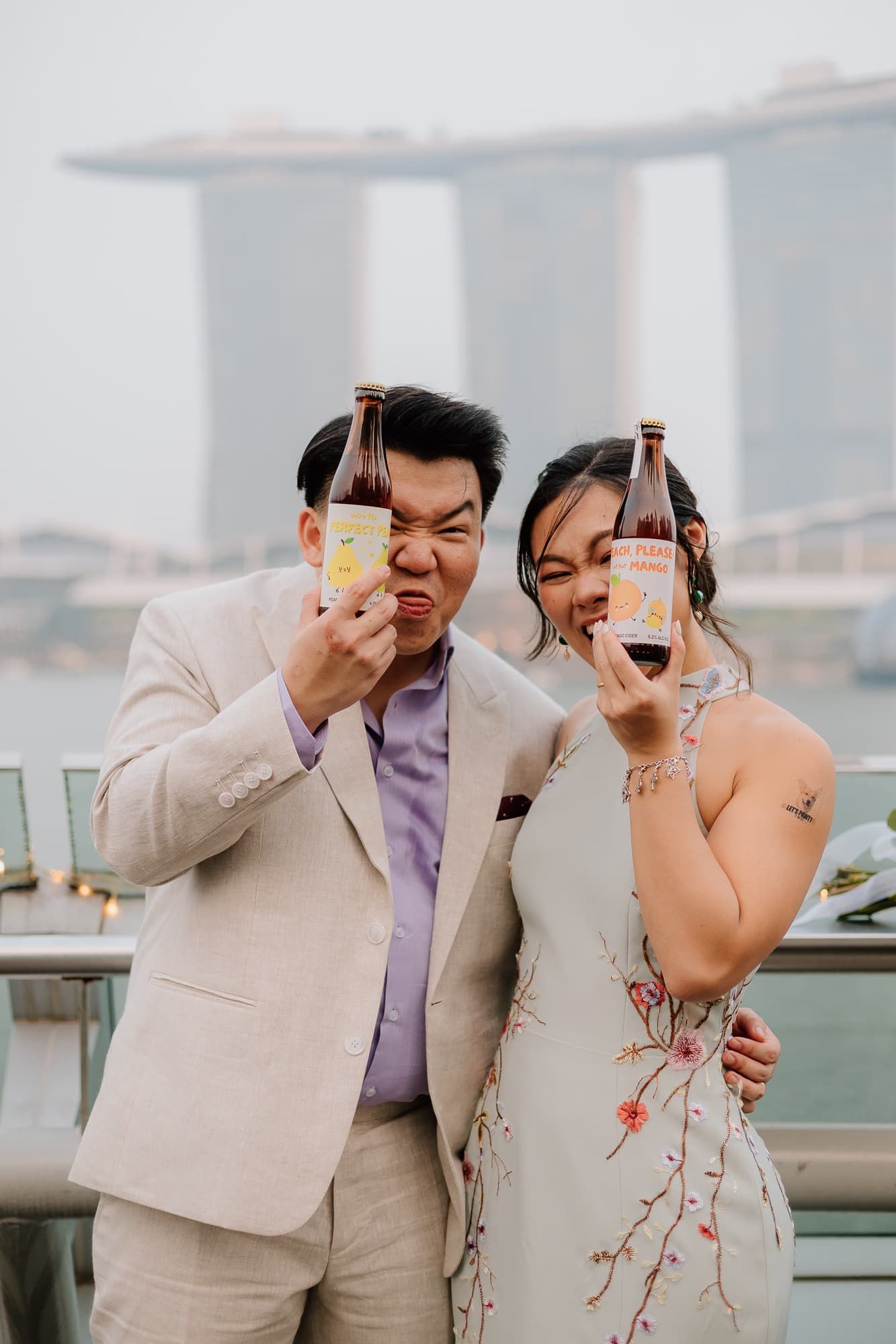 Couple celebrates with beverages against Singapore's Marina Bay Sands backdrop.