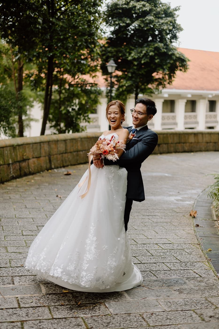 Joyful wedding couple shares tender moment on stone pathway during outdoor photoshoot.