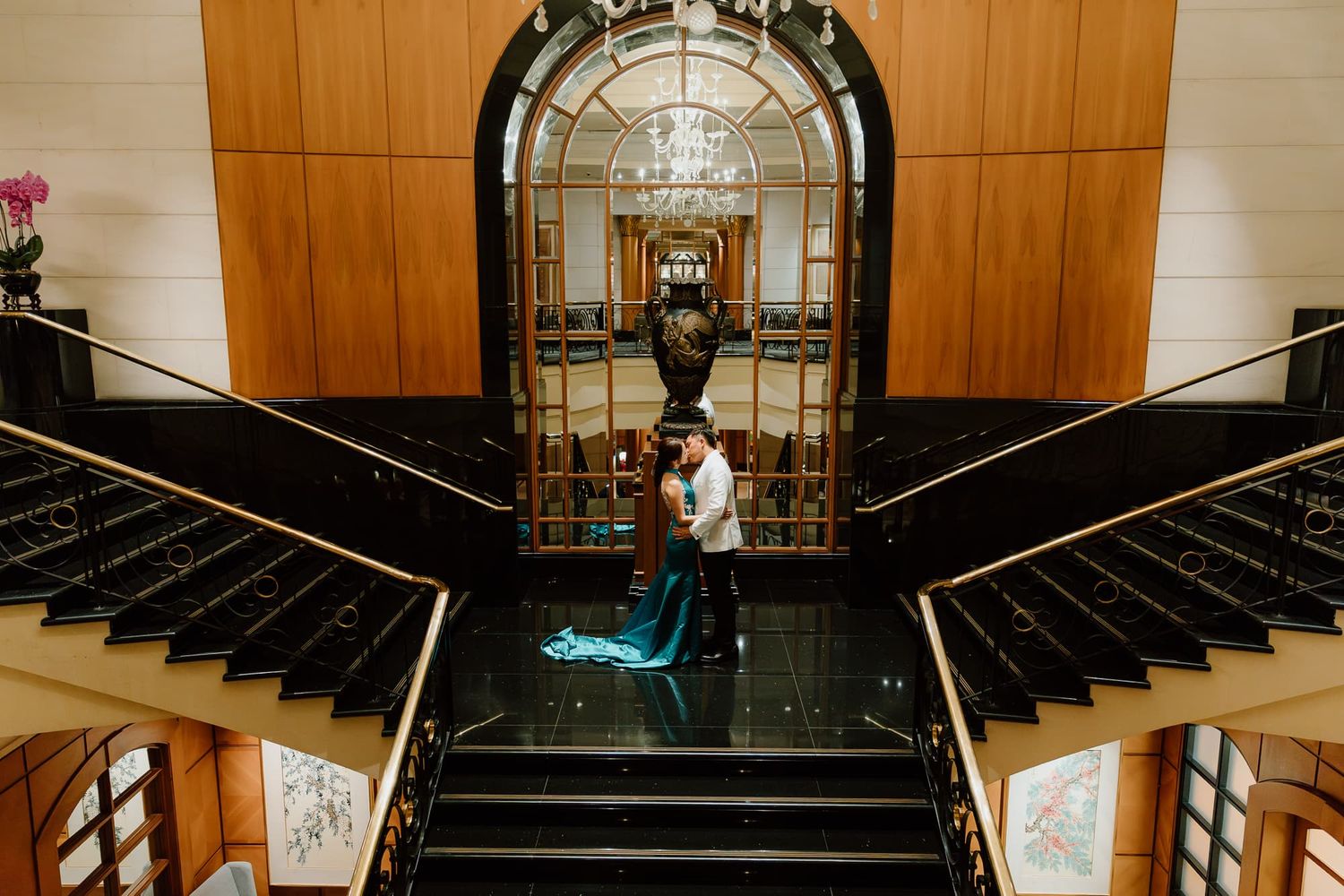 Elegant grand staircase with wood paneling and crystal chandelier in luxurious venue.