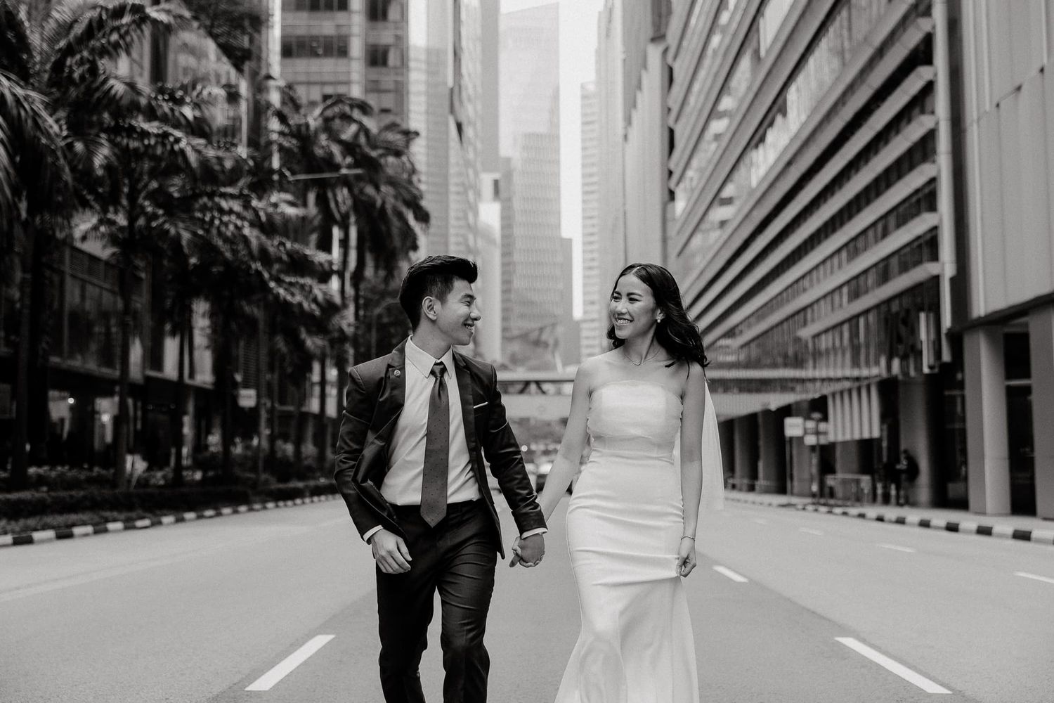 A bride and groom share a joyful moment while walking down an urban street in black and white.