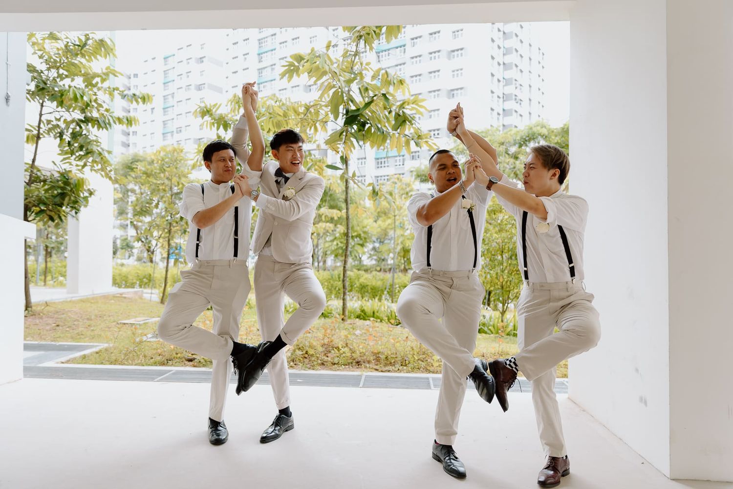 Wedding party members in matching white attire playfully interact in a modern hallway setting.