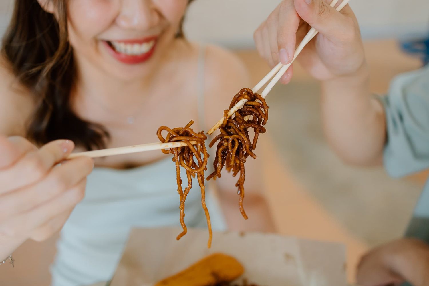 Chopsticks lifting up steaming noodles with a happy smile in the background.