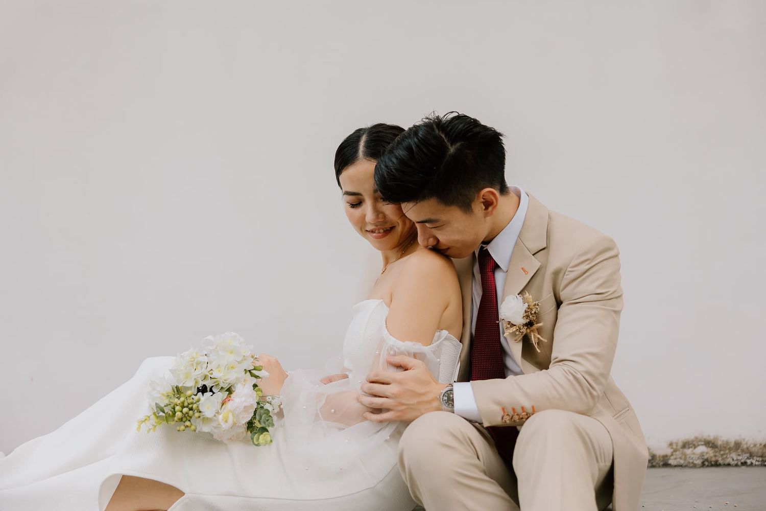 An intimate wedding portrait showing a tender embrace against a light background.