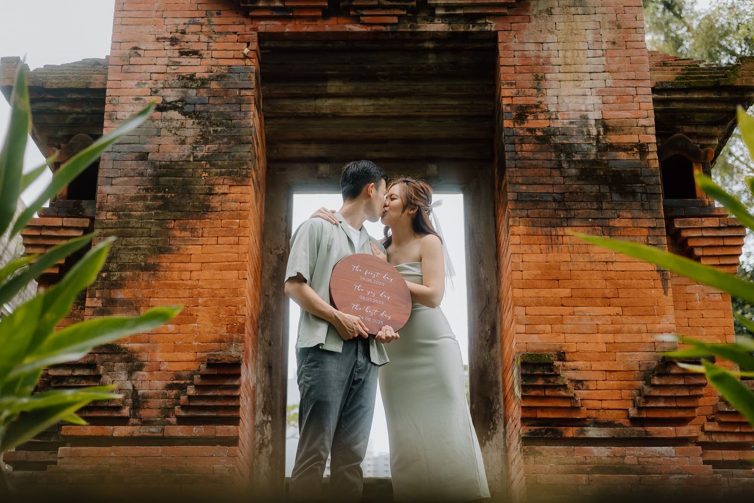 Couple embracing in a rustic brick doorway archway with tropical plants.