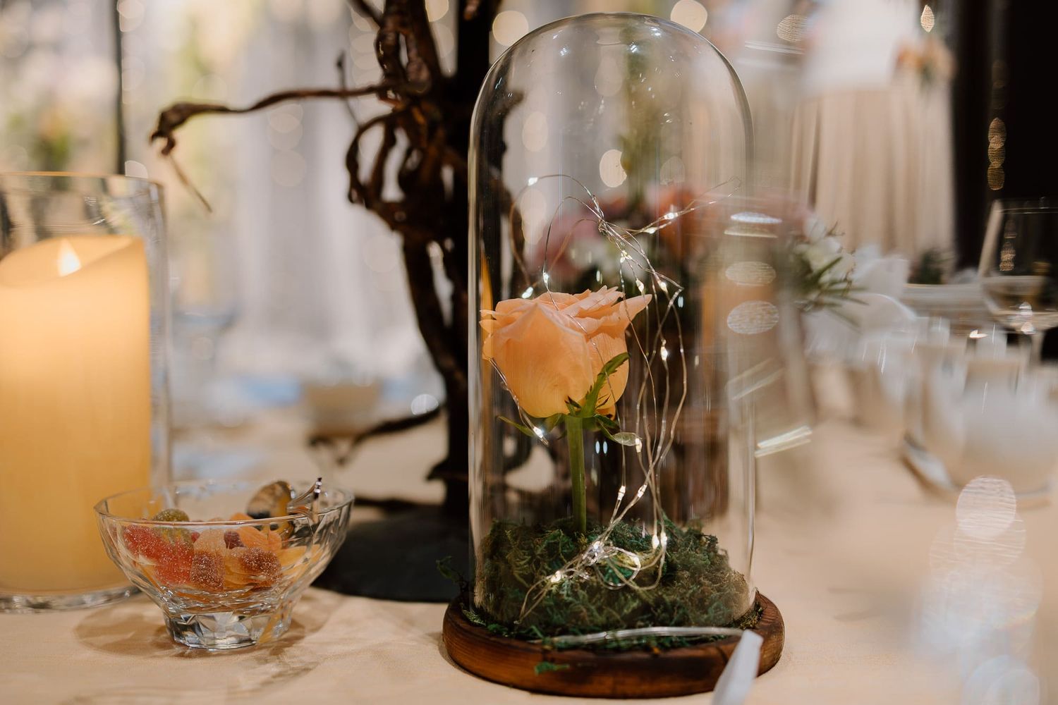 Wedding reception table decorated with elegant candles, greenery and wine glasses in warm evening light.