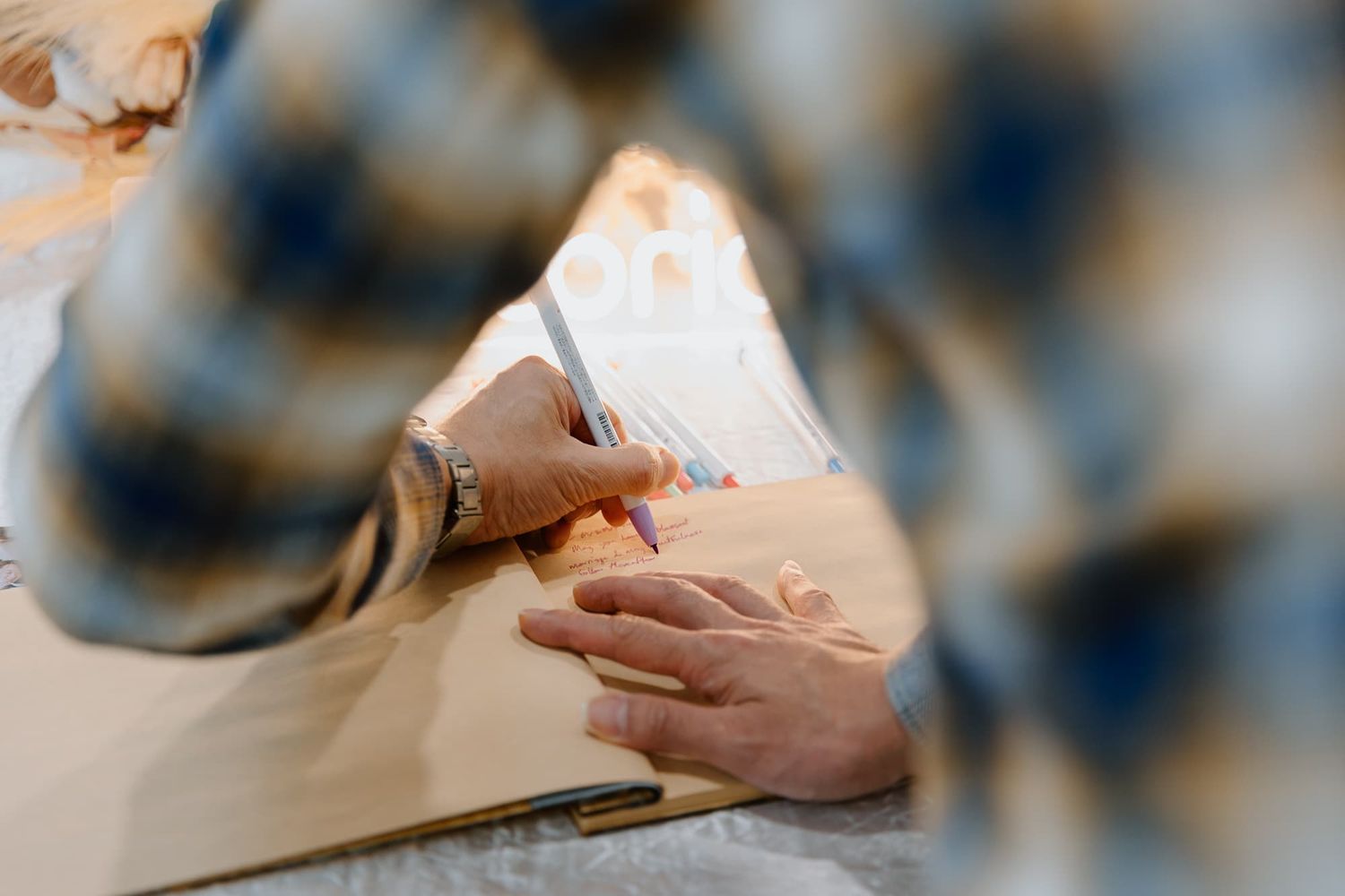 Close-up of hands writing in a guest book at a formal event.
