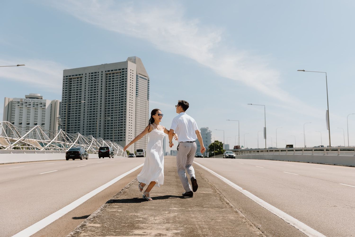 Couple holding hands while walking on a concrete path with urban skyline behind them.
