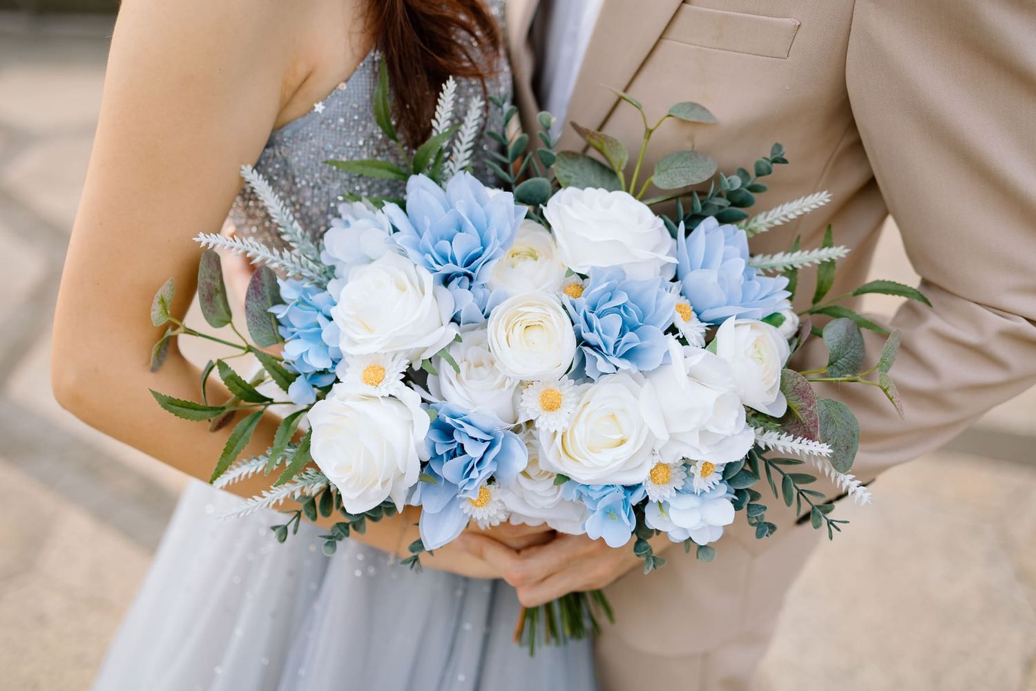 A stunning blue and white wedding bouquet with roses and hydrangeas held against a grey dress.