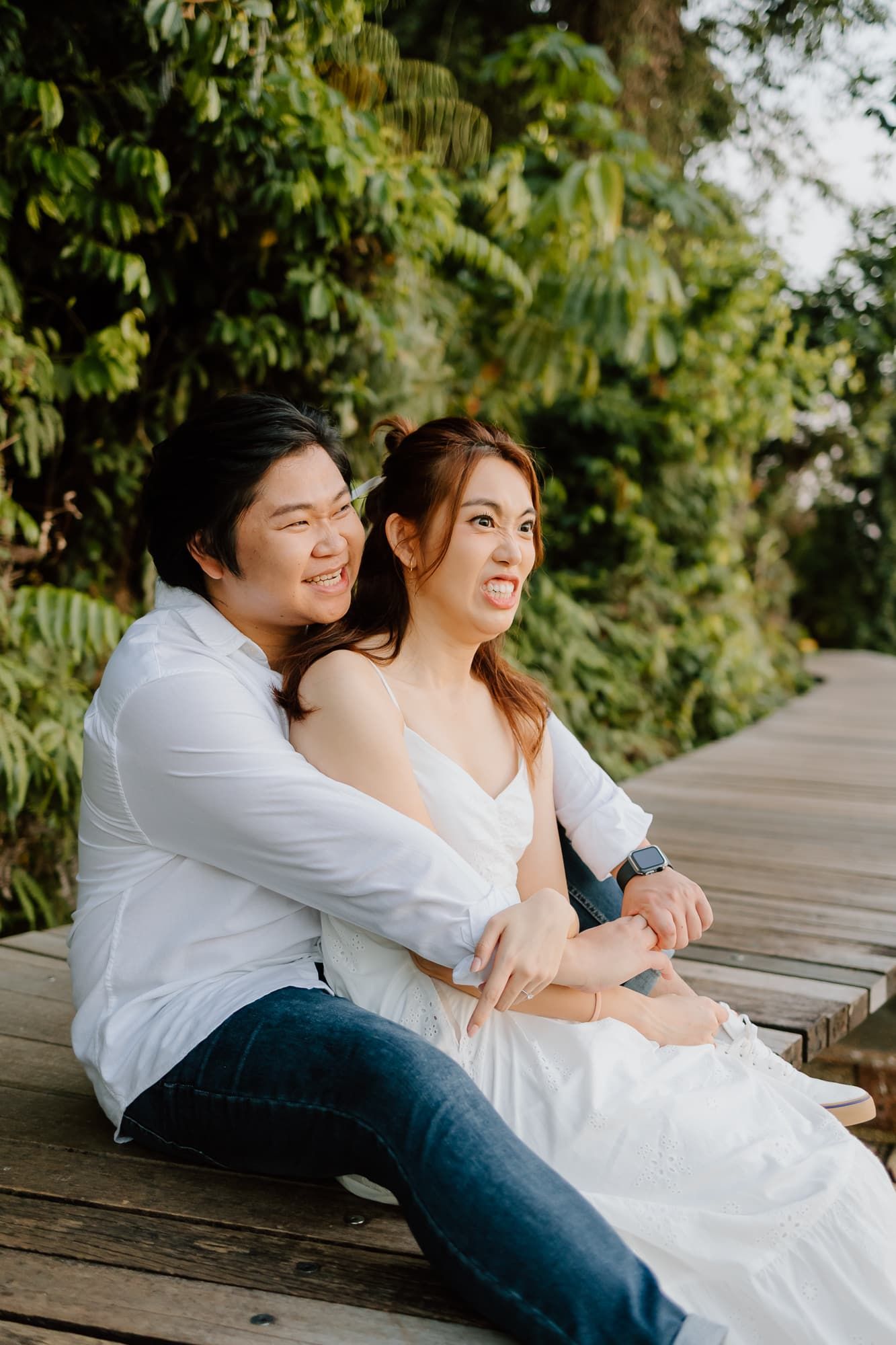Couple embracing on wooden deck surrounded by lush green foliage.
