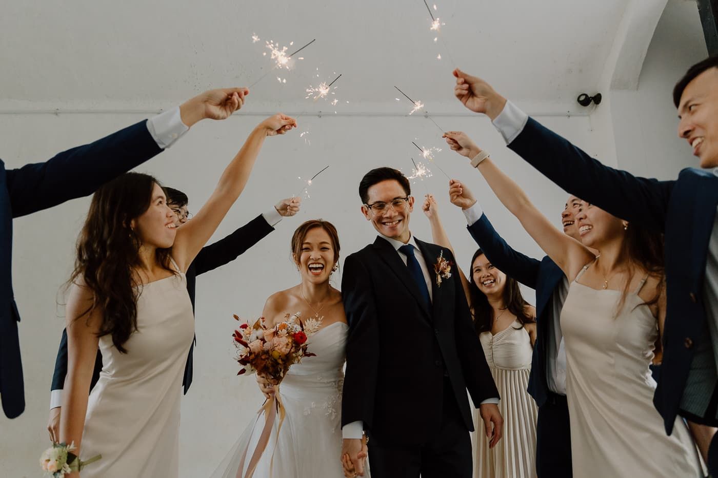 Wedding party celebrates with raised champagne glasses during joyful reception moment.