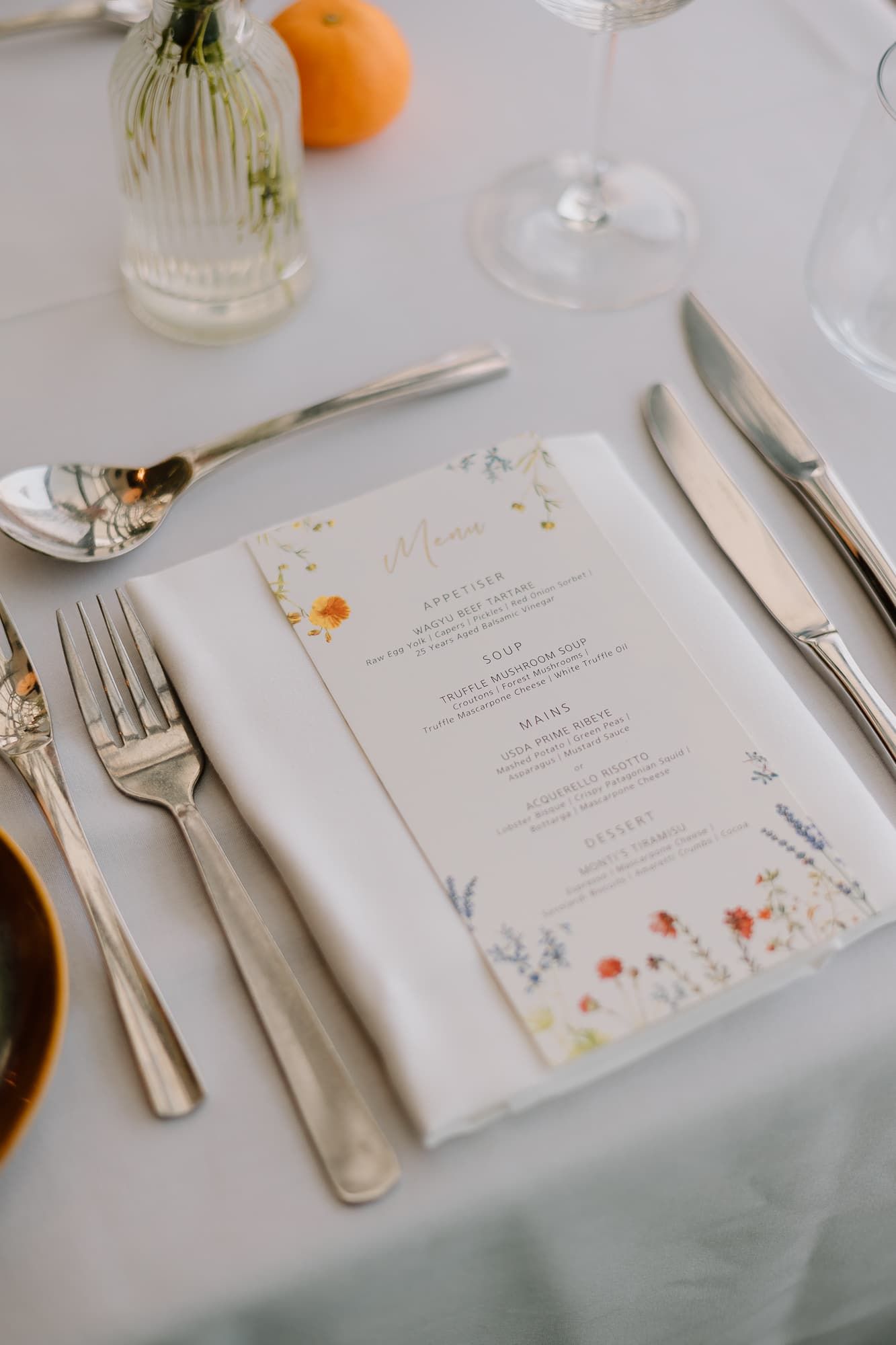 Wedding reception place setting with floral menu card and elegant silverware.