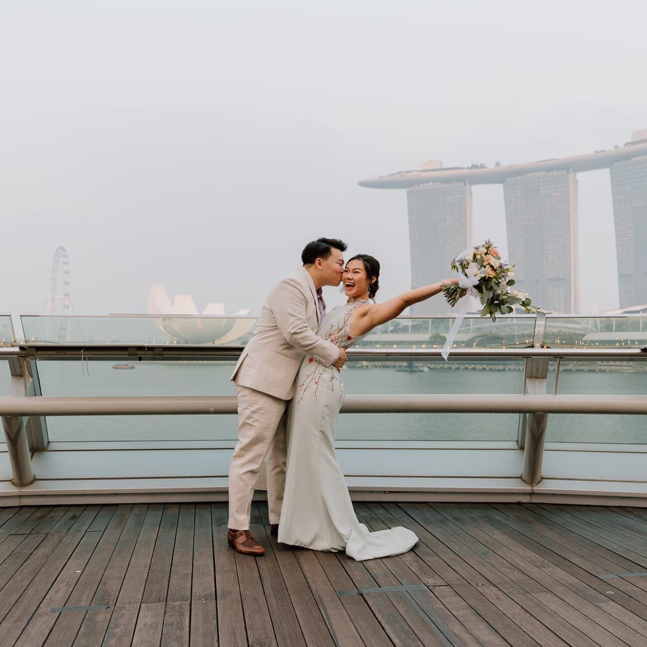 A romantic couple embraces on a rooftop deck with Marina Bay Sands visible in the background.