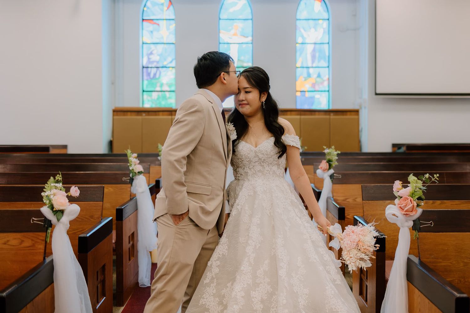 Couple shares intimate moment under stained glass windows in church sanctuary.