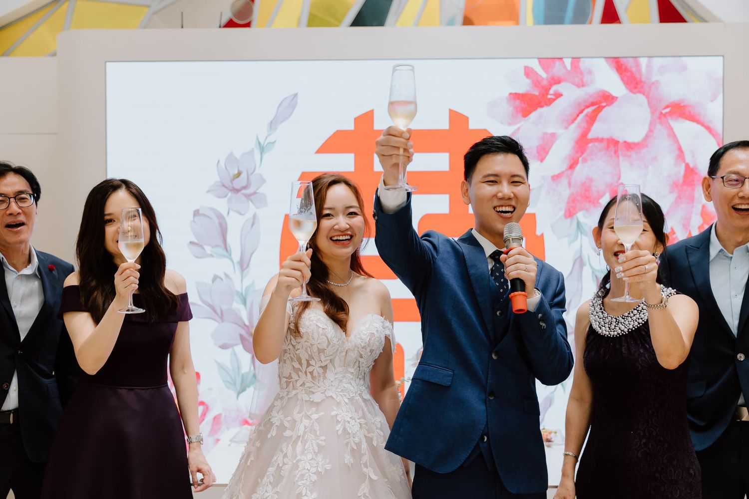 Wedding party celebrating with drinks in front of red and pink floral backdrop.