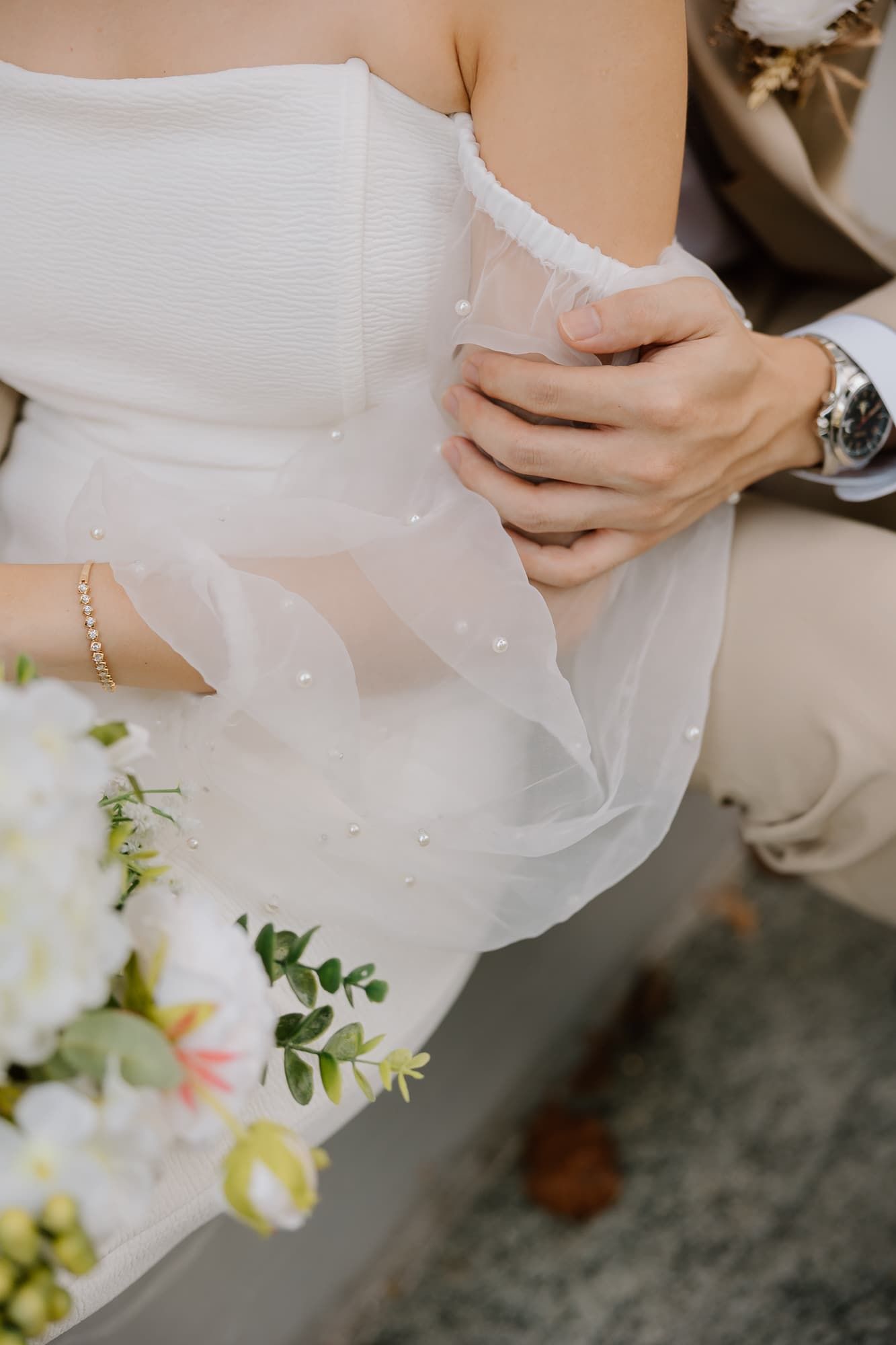 Close-up detail of delicate wedding dress fabric and bouquet with white flowers.