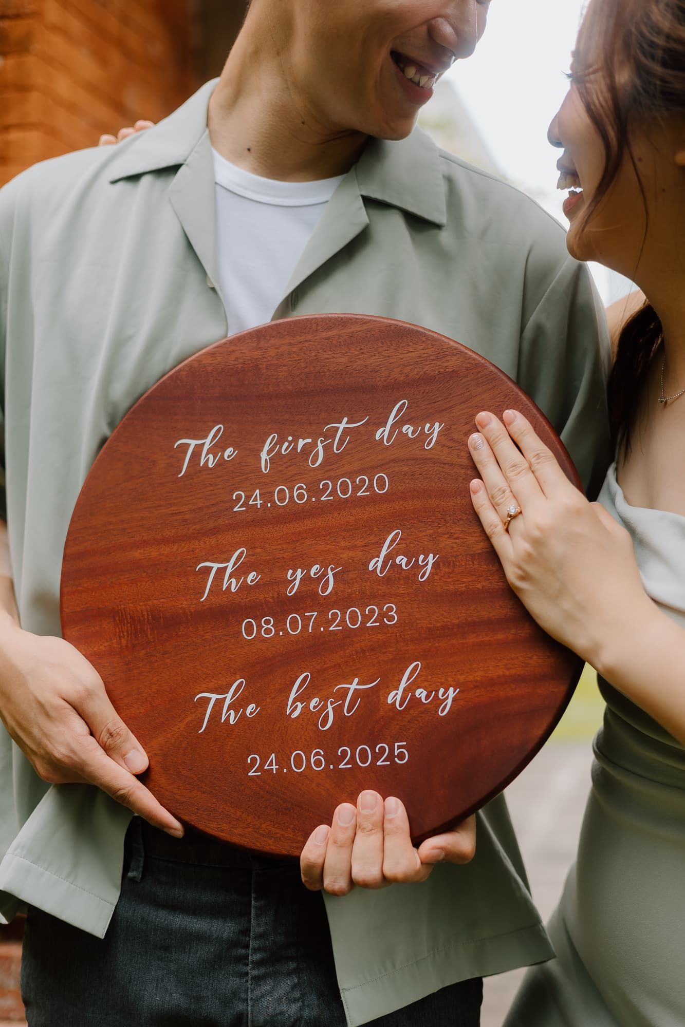 Close-up of wooden sign showing three special dates being held by a couple.